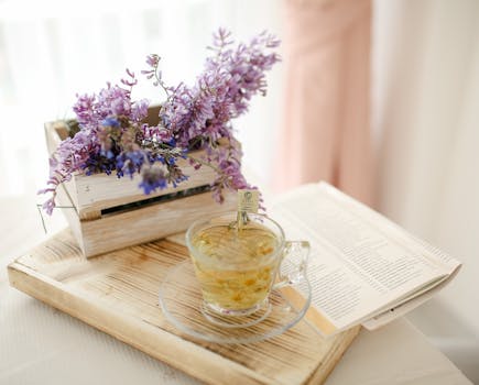 A peaceful setting featuring a glass cup of herbal tea, open book, and purple flowers.